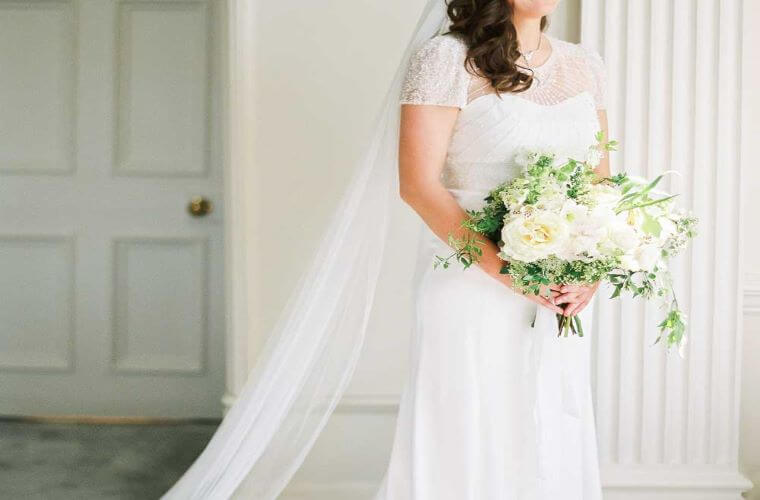The torso of a bride in a white dress holding a bouquet of white flowers